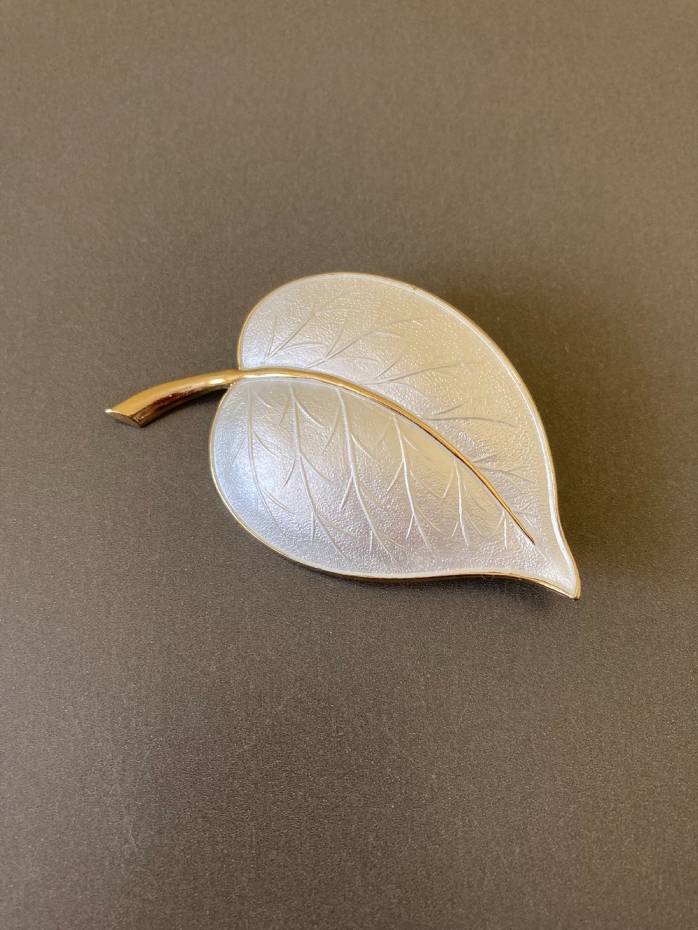 A leaf-shaped white guilloche enamel brooch with silver gilt edges and a curved stem. View II