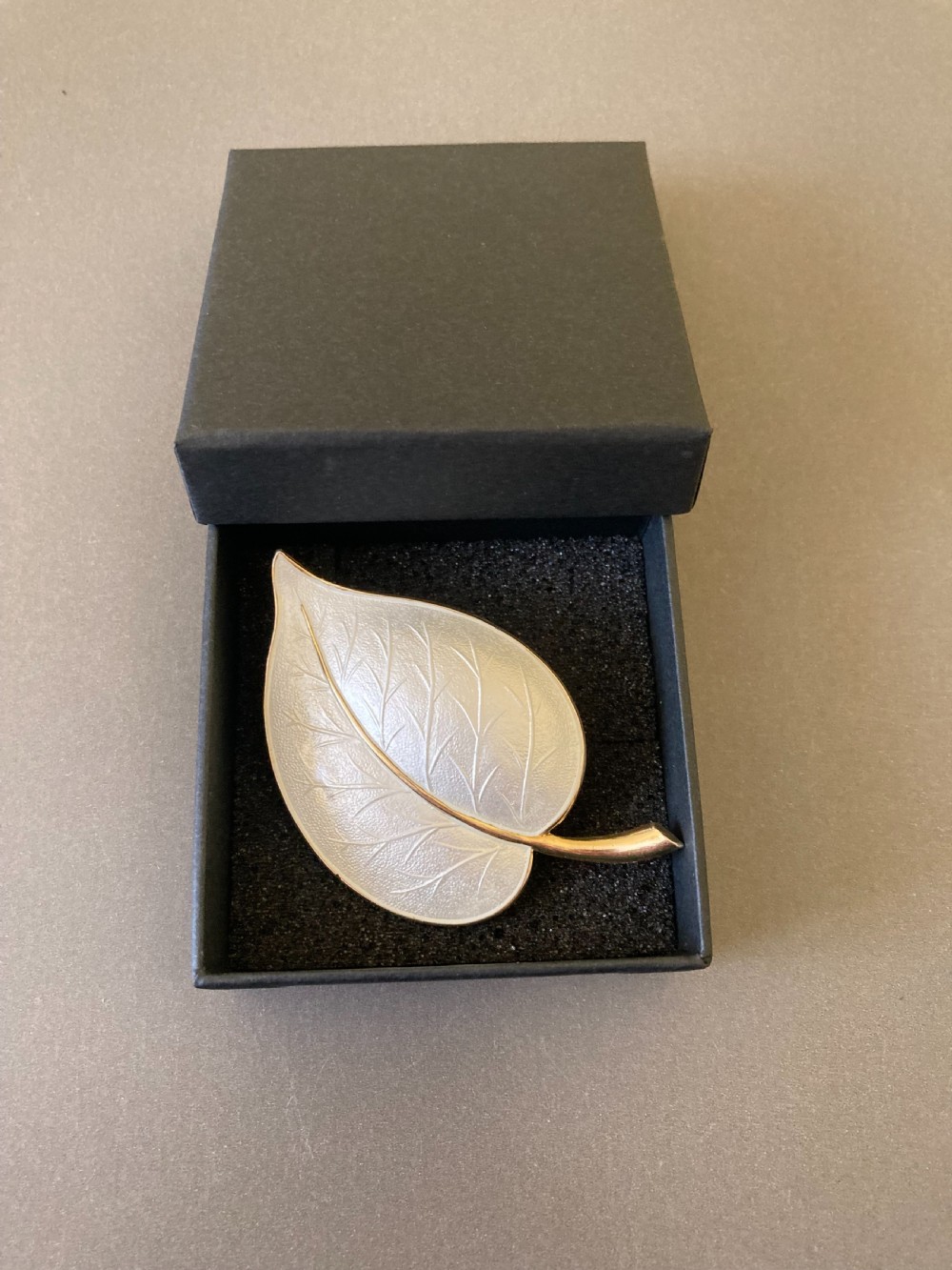 A leaf-shaped white guilloche enamel brooch with silver gilt edges and a curved stem. View VI