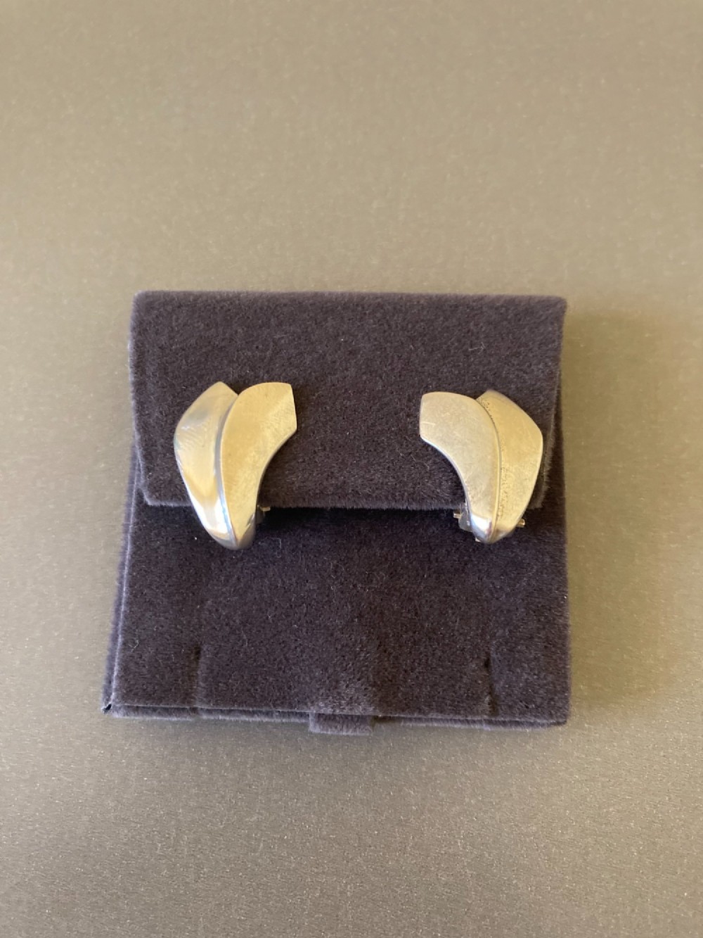 A pair of Georg Jensen Danish sterling silver lotus leaf clip-on earrings displayed on a dark grey velvet pouch.