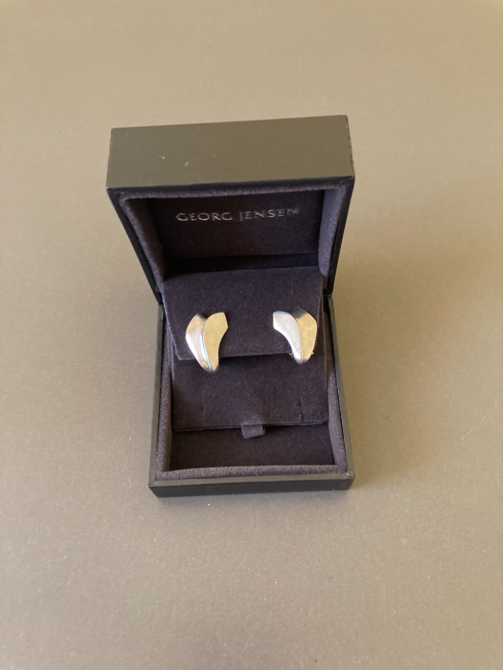 A pair of Georg Jensen Danish sterling silver lotus leaf clip-on earrings displayed on a dark grey velvet pouch. View III