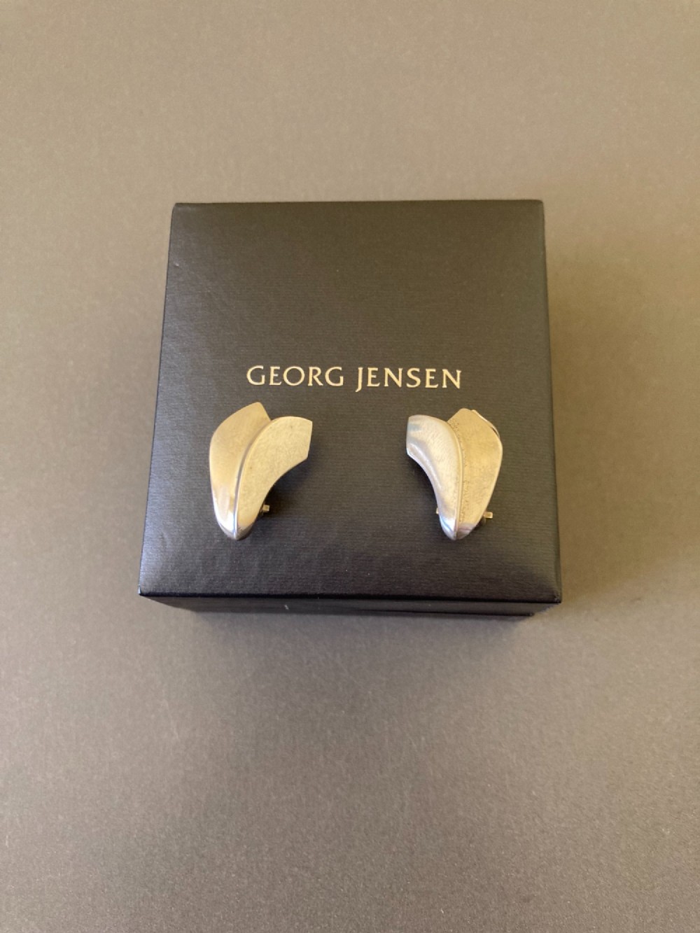 A pair of Georg Jensen Danish sterling silver lotus leaf clip-on earrings displayed on a dark grey velvet pouch. View V