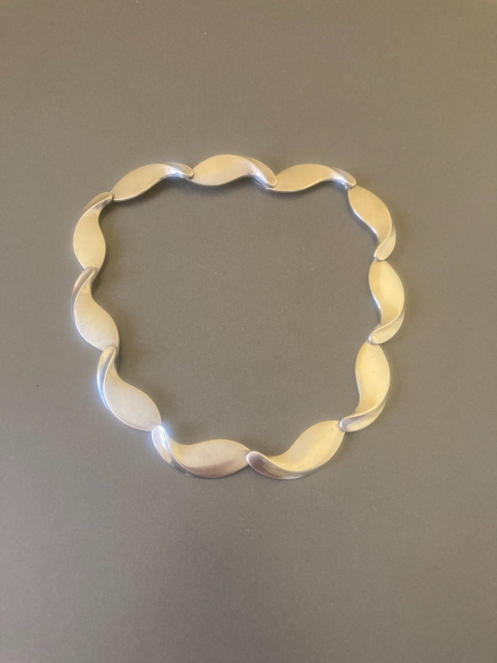 A Georg Jensen 1960s Danish sterling silver necklace featuring contoured, wave-like articulated links arranged in a circular shape.
