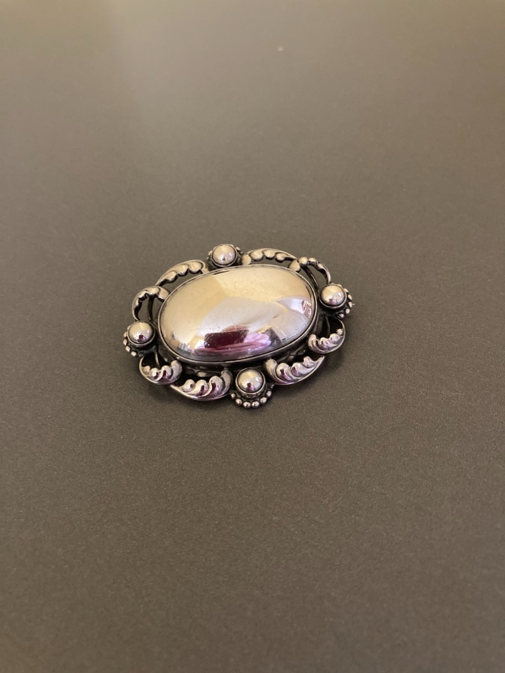 An oval sterling silver brooch featuring a central polished dome bordered by openwork leaf scrolls and beaded accents. View II