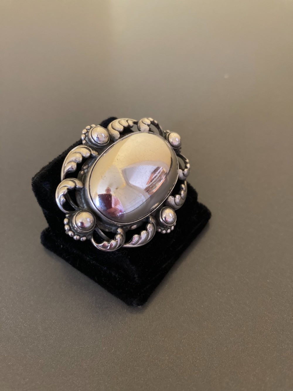 An oval sterling silver brooch featuring a central polished dome bordered by openwork leaf scrolls and beaded accents. View III