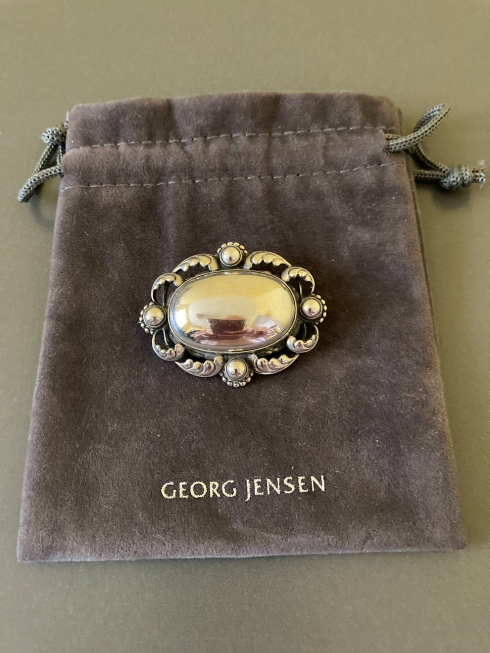 An oval sterling silver brooch featuring a central polished dome bordered by openwork leaf scrolls and beaded accents. View IV