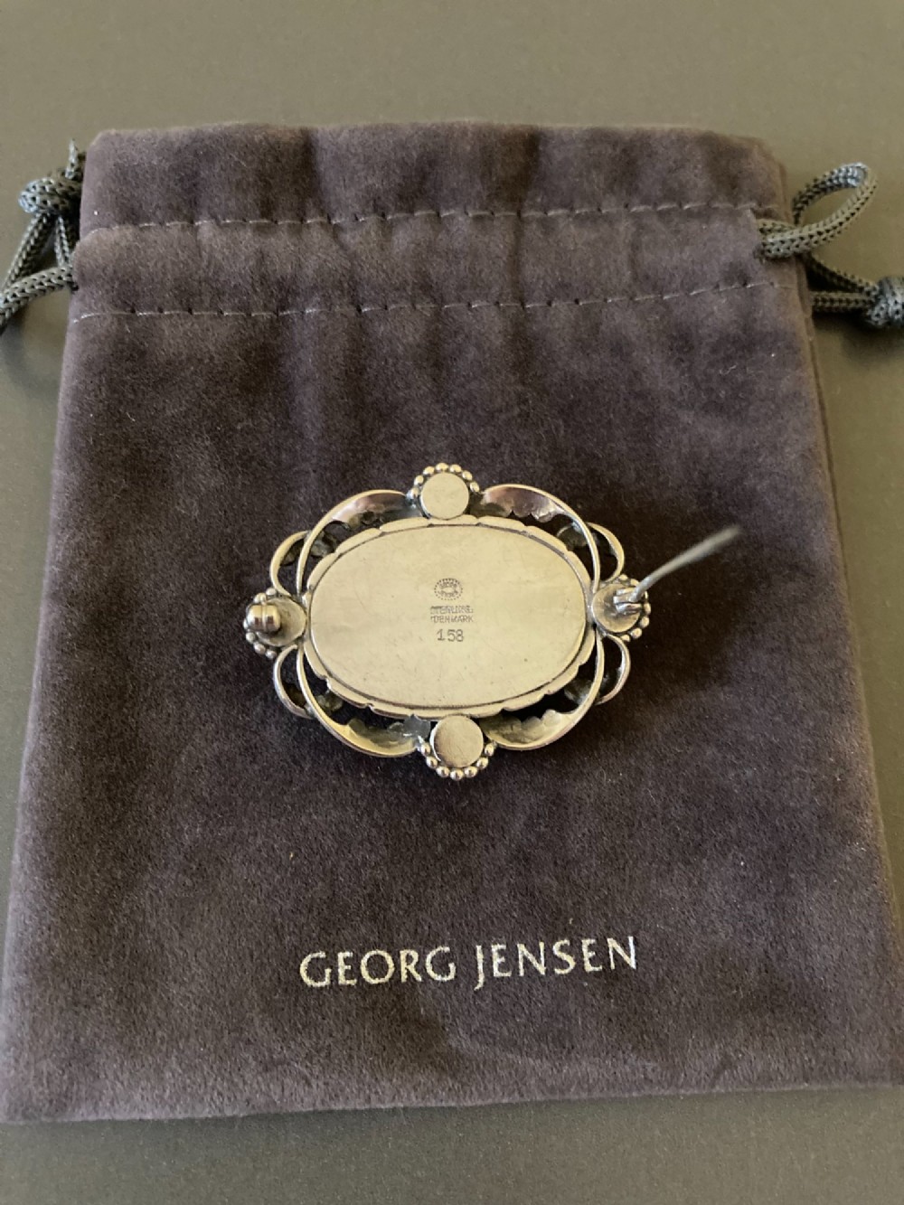 An oval sterling silver brooch featuring a central polished dome bordered by openwork leaf scrolls and beaded accents. View V