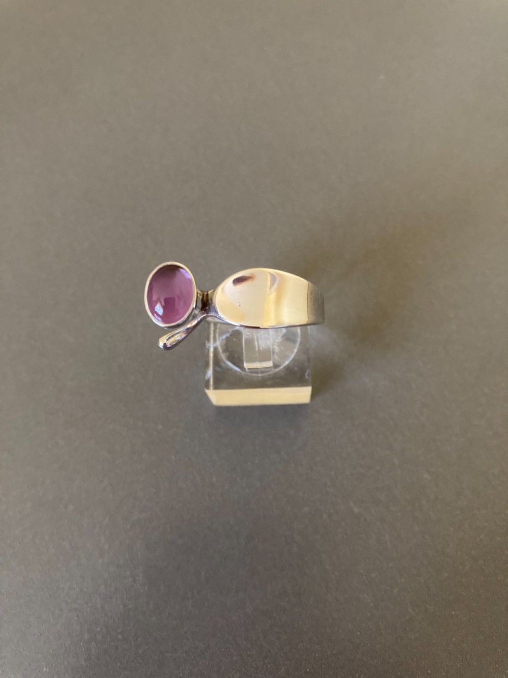 A sterling silver ring featuring a fluid organic band set with an offset oval purple cabochon amethyst.