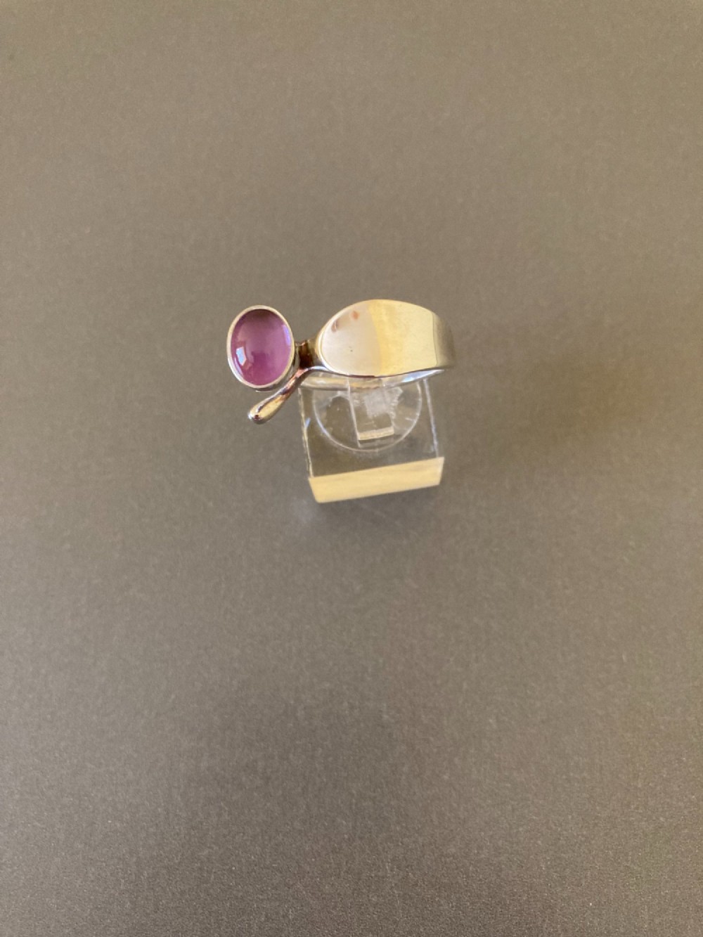 A sterling silver ring featuring a fluid organic band set with an offset oval purple cabochon amethyst. View V