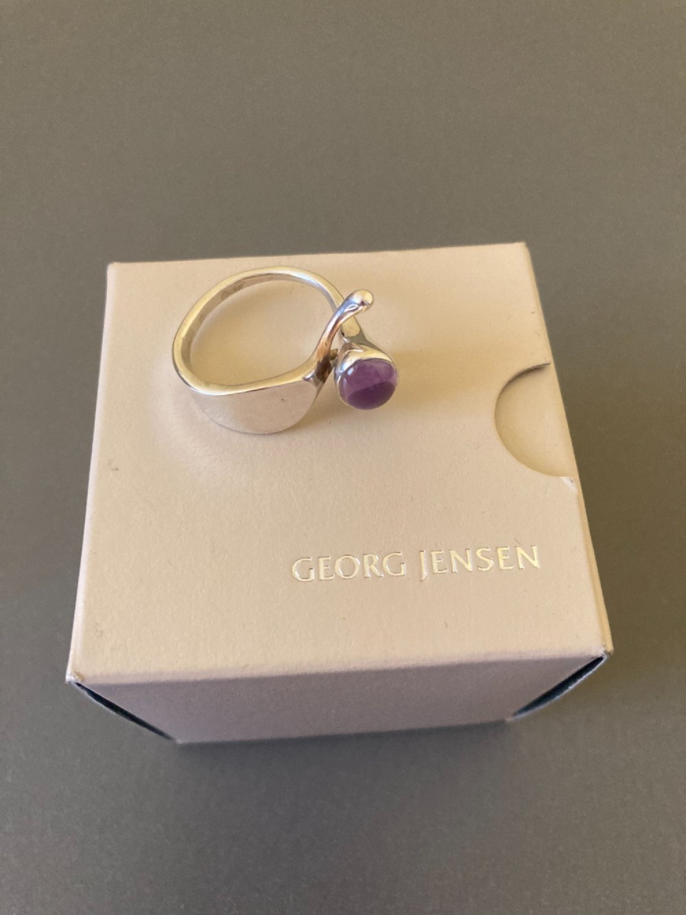 A sterling silver ring featuring a fluid organic band set with an offset oval purple cabochon amethyst. View VII