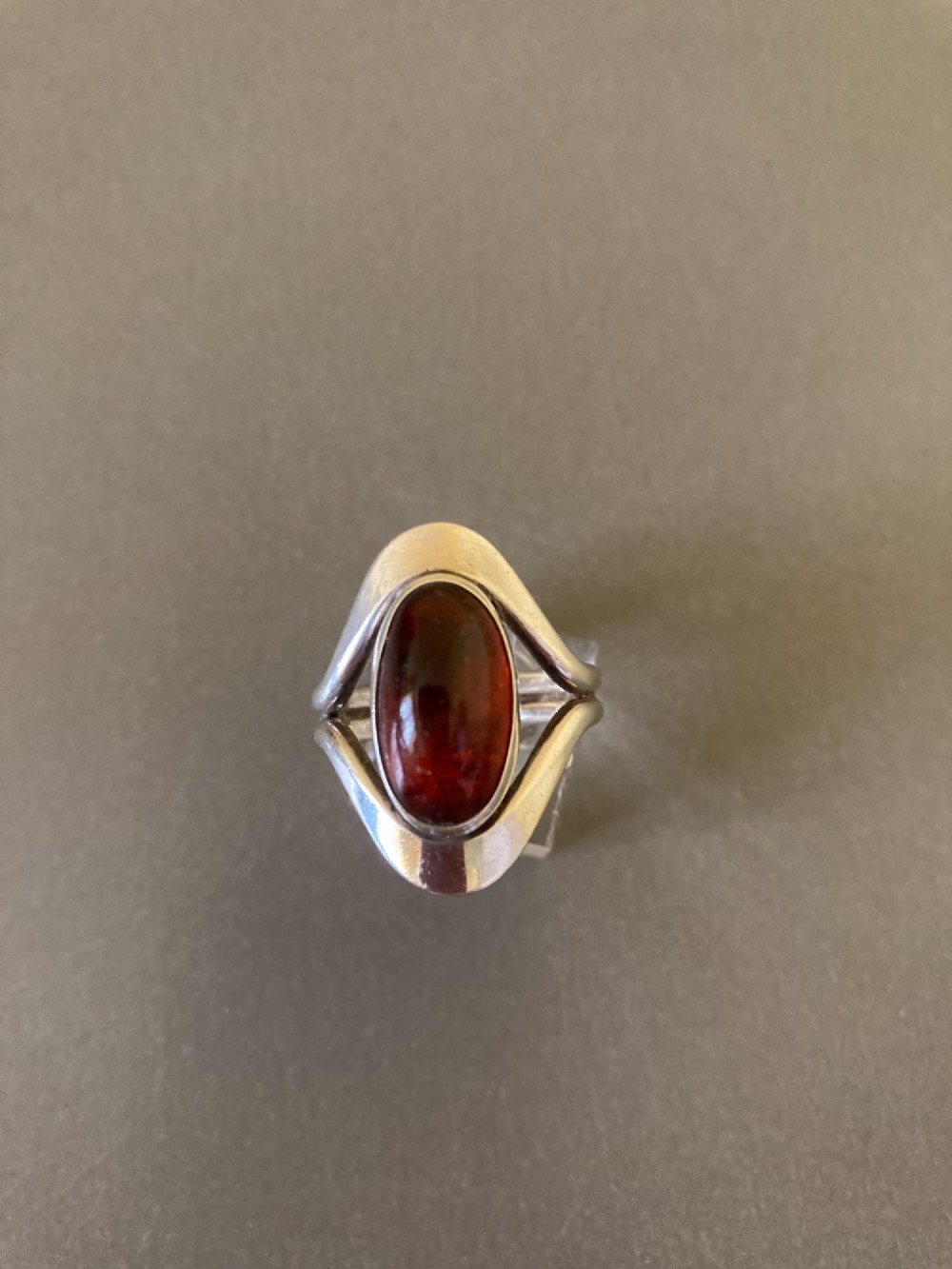 A mid-century Danish sterling silver ring featuring a central oval cabochon amber stone enclosed within a sculptural split-band frame. View IV