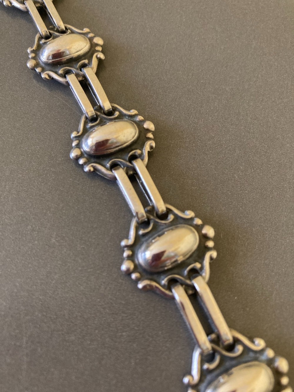 A 1930s Danish silver link bracelet featuring seven raised oval cabochon motifs surrounded by scrollwork borders and joined by parallel bar links. View II