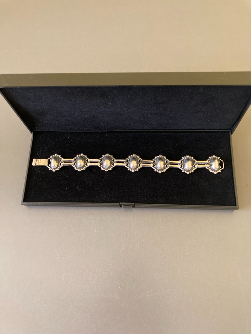 A 1930s Danish silver link bracelet featuring seven raised oval cabochon motifs surrounded by scrollwork borders and joined by parallel bar links. View IV