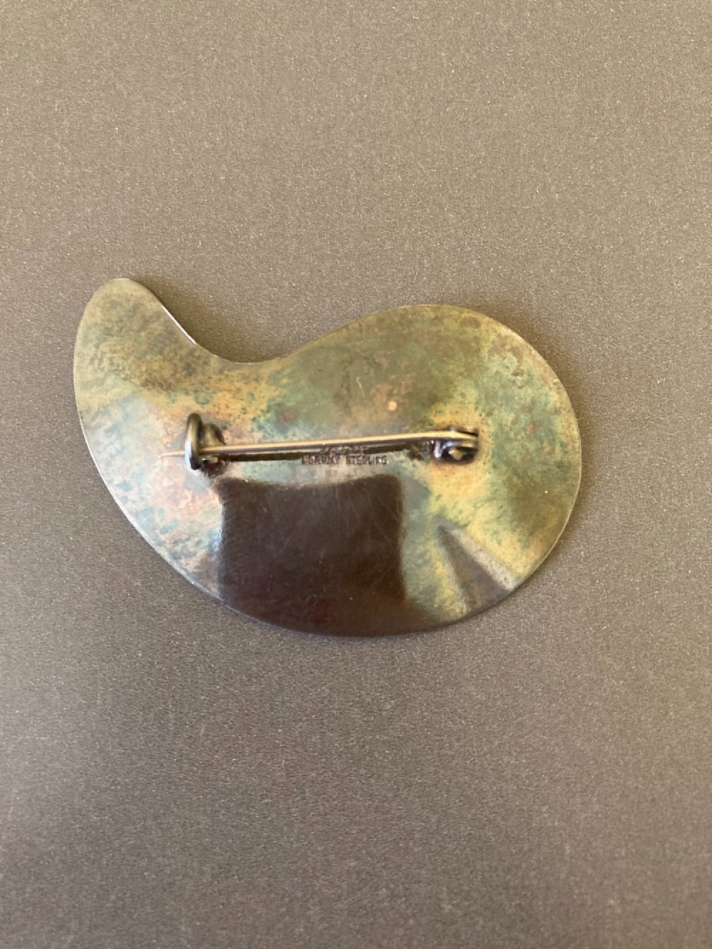 A silver brooch shaped like an artists palette with a black enamel background and five colourful enamel paint swatches. View IV