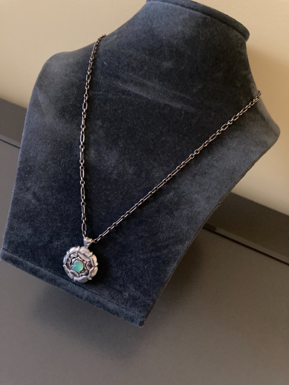 A circular sterling silver pendant with relief floral petal detailing and a central green cabochon chrysoprase, hanging from a silver link chain. View II