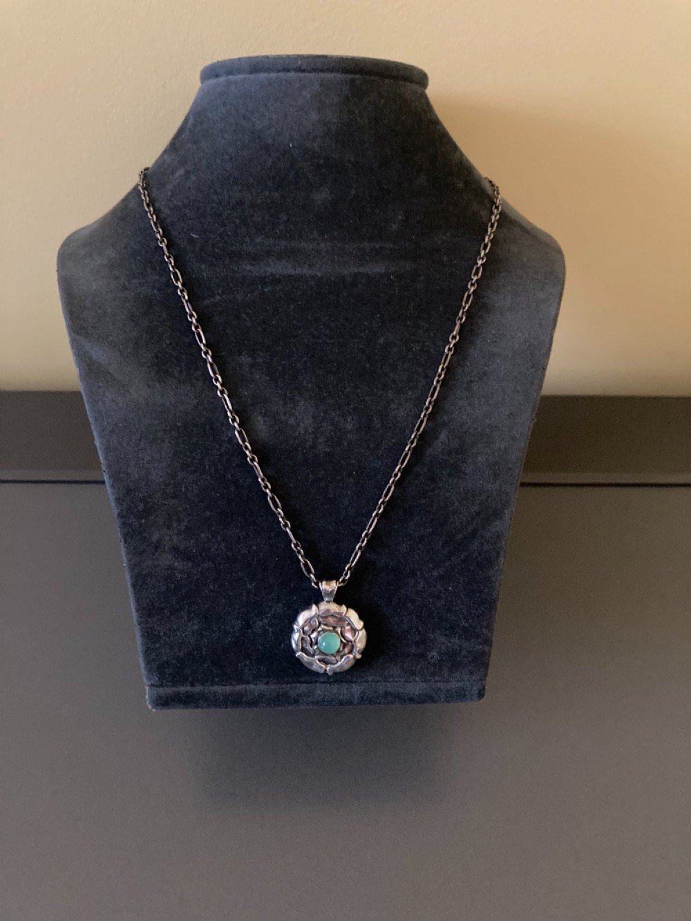 A circular sterling silver pendant with relief floral petal detailing and a central green cabochon chrysoprase, hanging from a silver link chain. View III