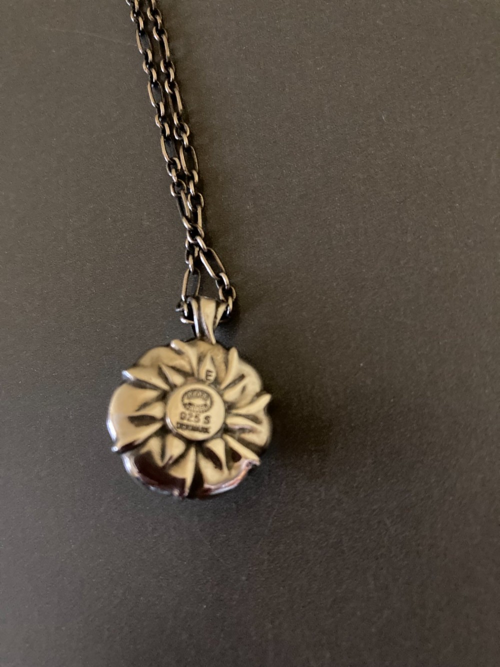 A circular sterling silver pendant with relief floral petal detailing and a central green cabochon chrysoprase, hanging from a silver link chain. View V
