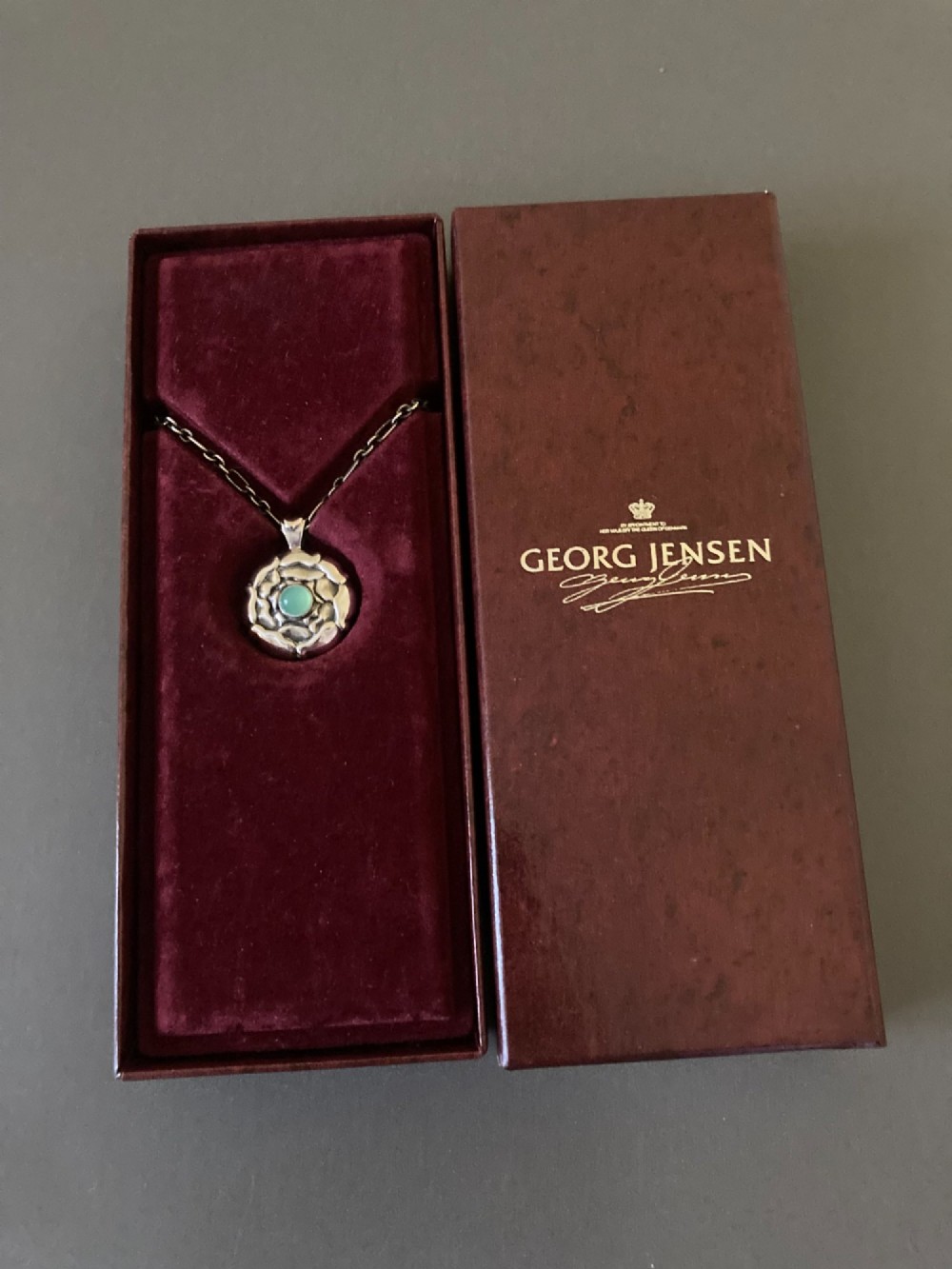 A circular sterling silver pendant with relief floral petal detailing and a central green cabochon chrysoprase, hanging from a silver link chain. View VI
