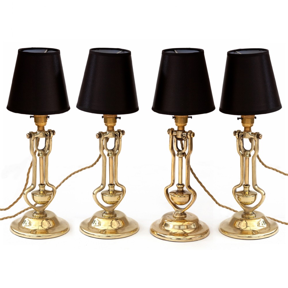 A set of four polished brass gimbal table lamps featuring articulated counterweighted frames and black fabric shades.