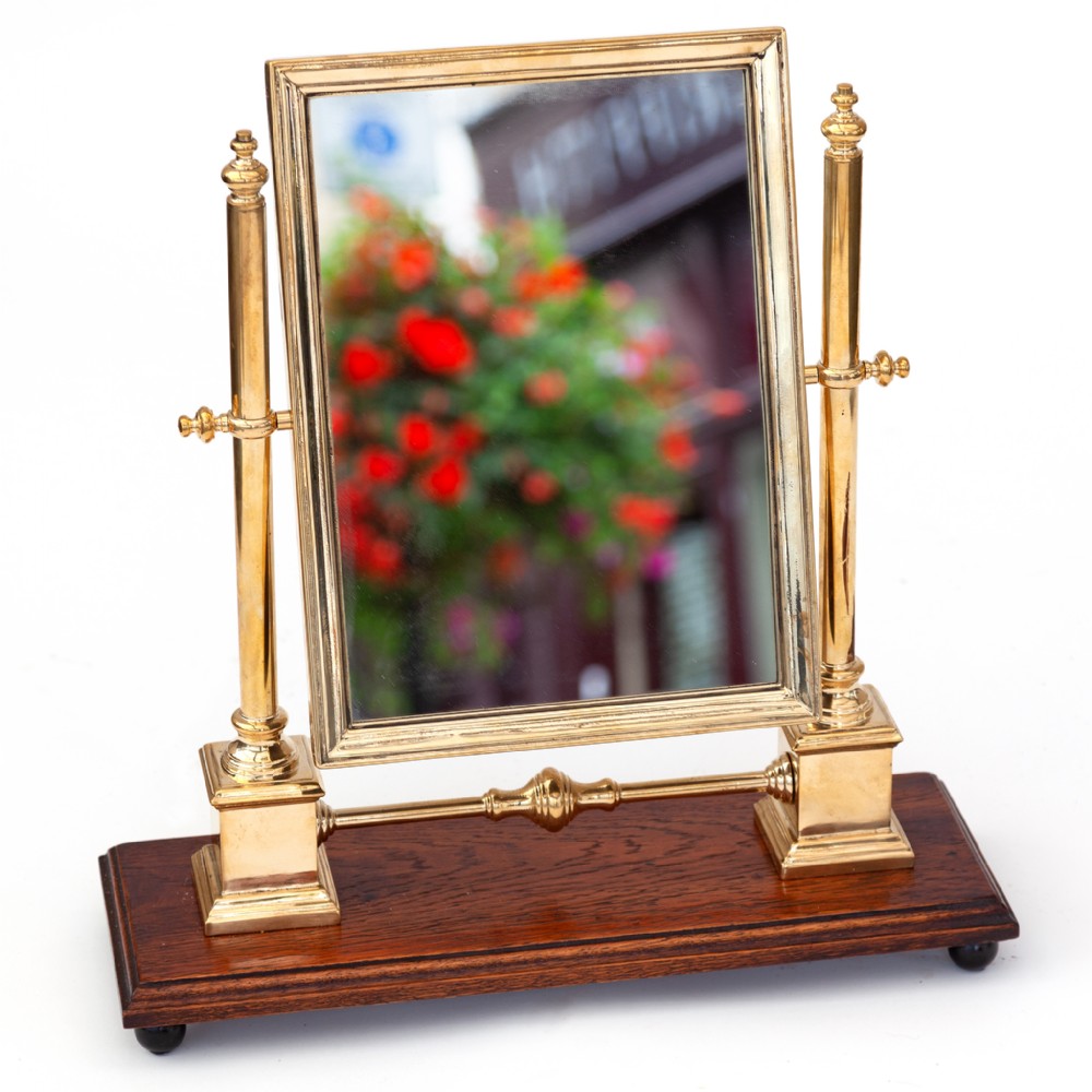 A rectangular brass-framed swivelling mirror supported by two brass columns on a dark polished oak base.