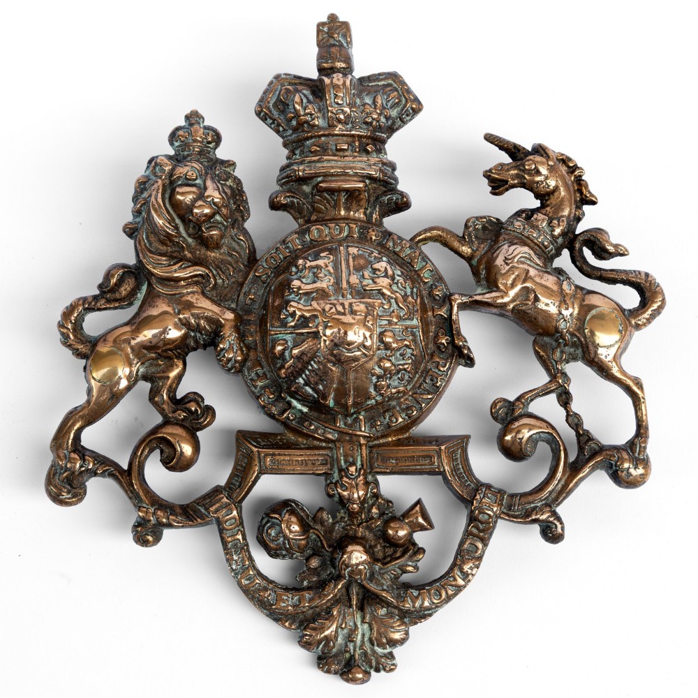 A cast brass wall plaque depicting the British Royal Coat of Arms featuring a lion and unicorn flanking a central shield and crown.