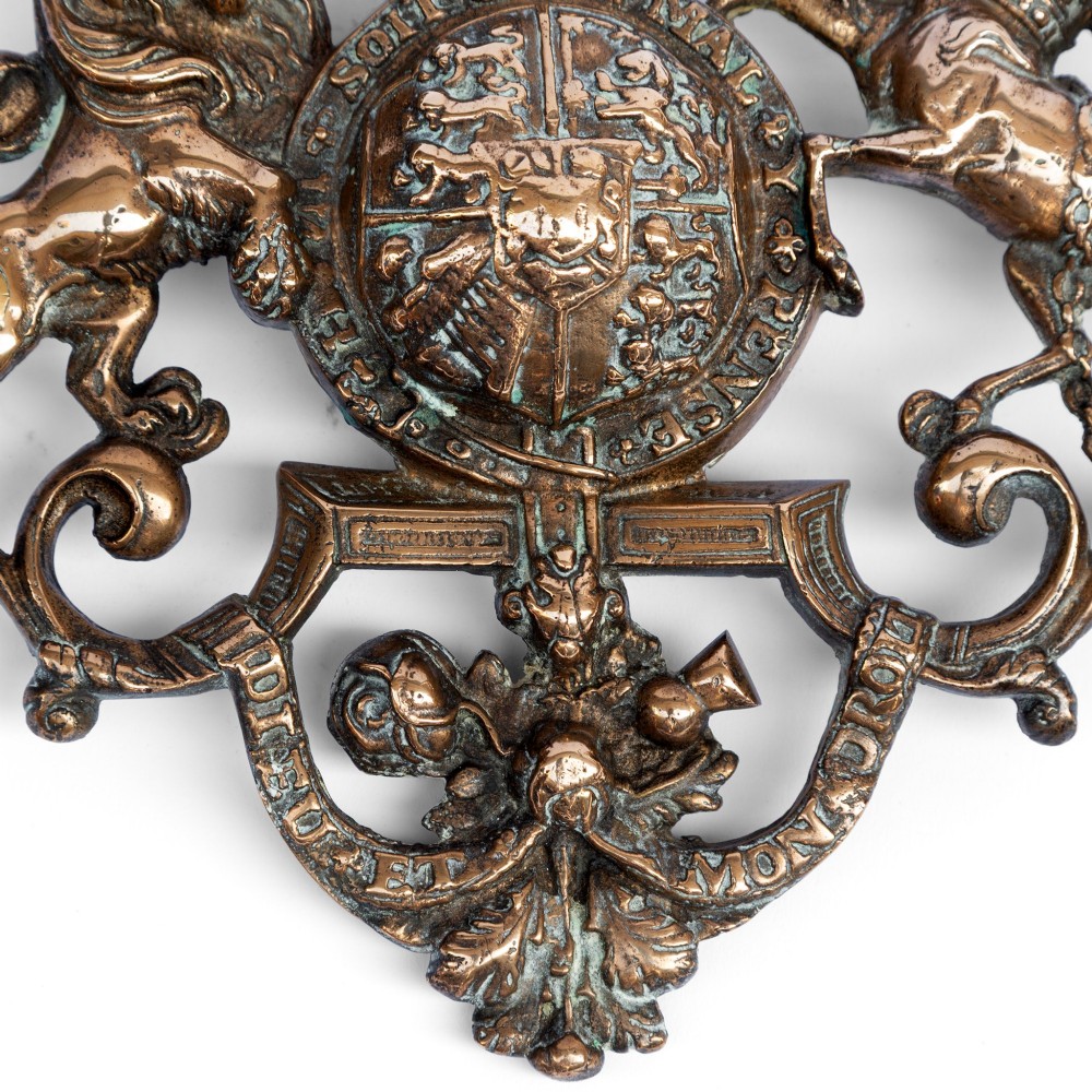 A cast brass wall plaque depicting the British Royal Coat of Arms featuring a lion and unicorn flanking a central shield and crown. View IV