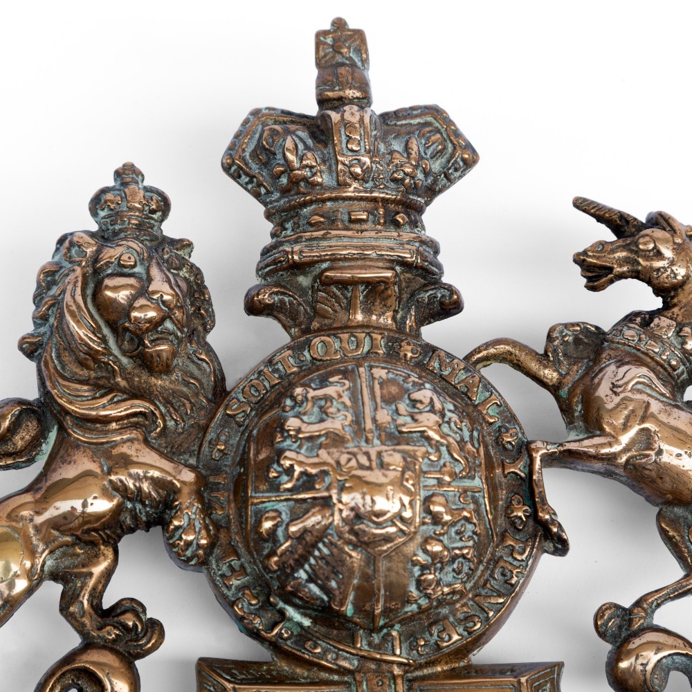 A cast brass wall plaque depicting the British Royal Coat of Arms featuring a lion and unicorn flanking a central shield and crown. View V