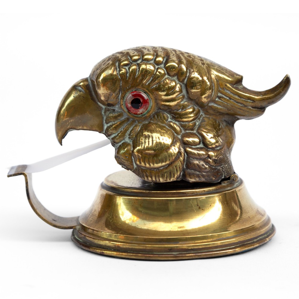 A cast brass desk tape dispenser formed in the shape of a parrot head with red glass eyes set on a round stepped base. View II