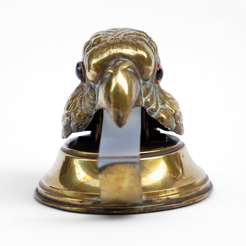 A cast brass desk tape dispenser formed in the shape of a parrot head with red glass eyes set on a round stepped base. View III
