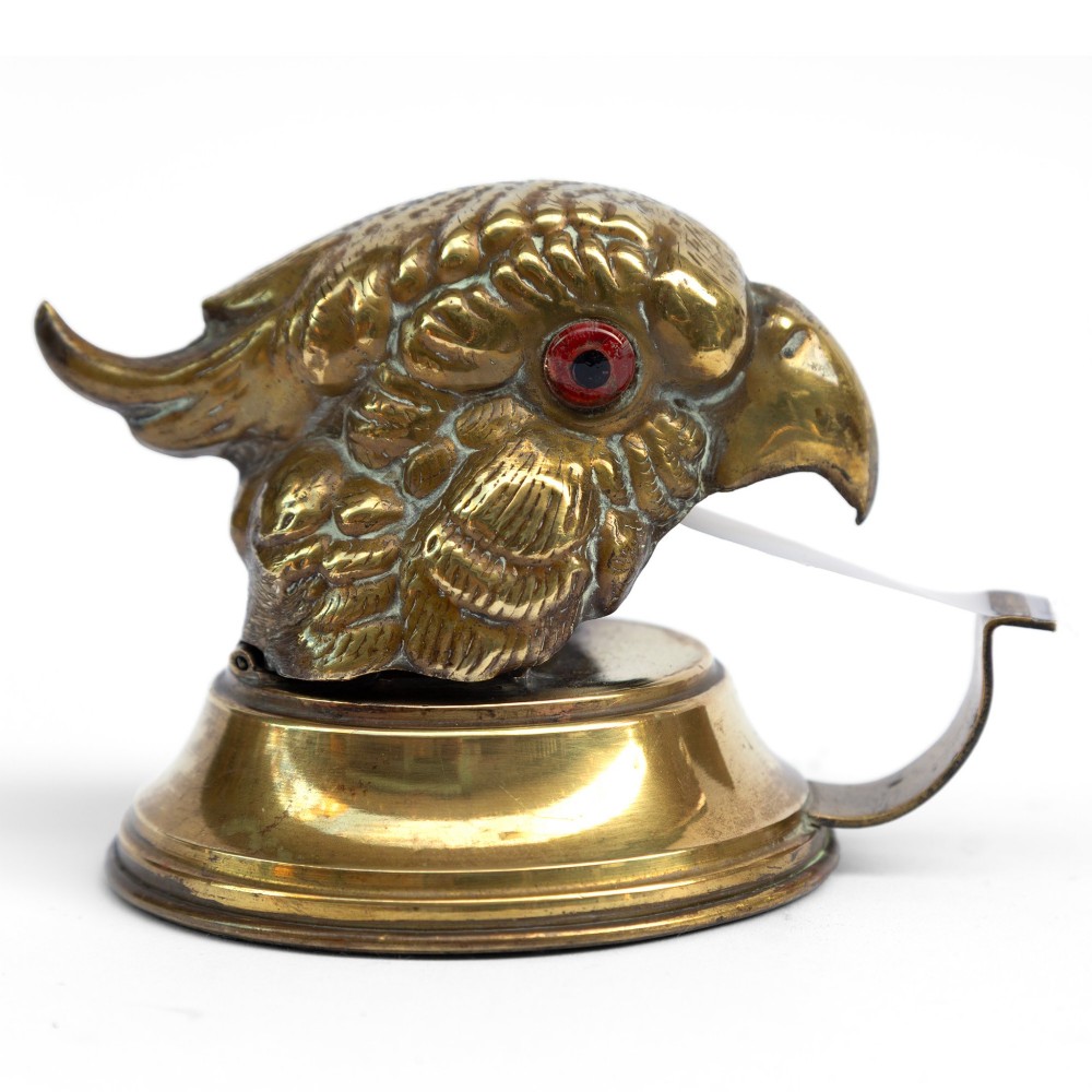 A cast brass desk tape dispenser formed in the shape of a parrot head with red glass eyes set on a round stepped base. View IV