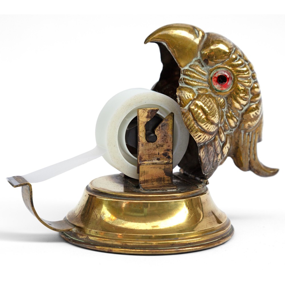 A cast brass desk tape dispenser formed in the shape of a parrot head with red glass eyes set on a round stepped base. View V