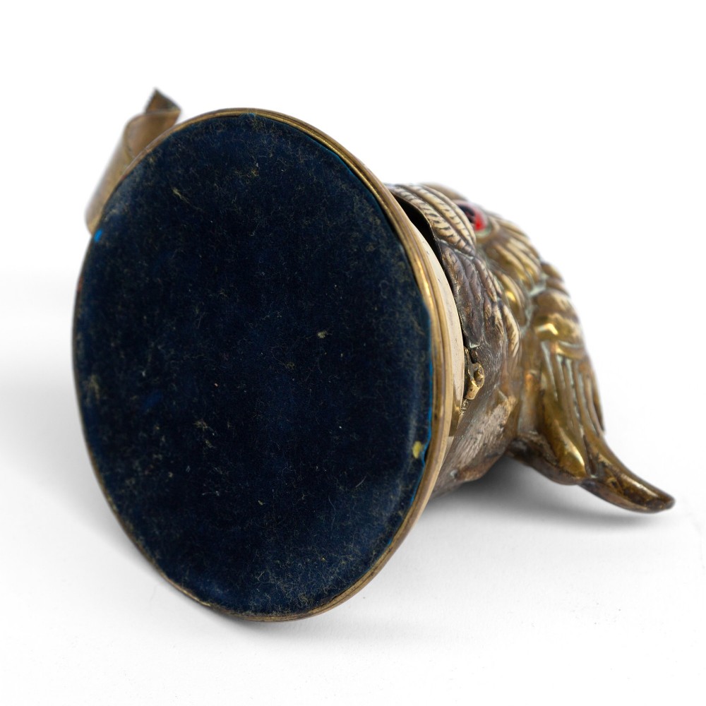 A cast brass desk tape dispenser formed in the shape of a parrot head with red glass eyes set on a round stepped base. View VII