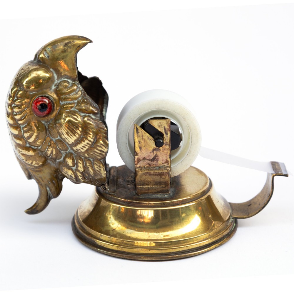 A cast brass desk tape dispenser formed in the shape of a parrot head with red glass eyes set on a round stepped base. View VIII