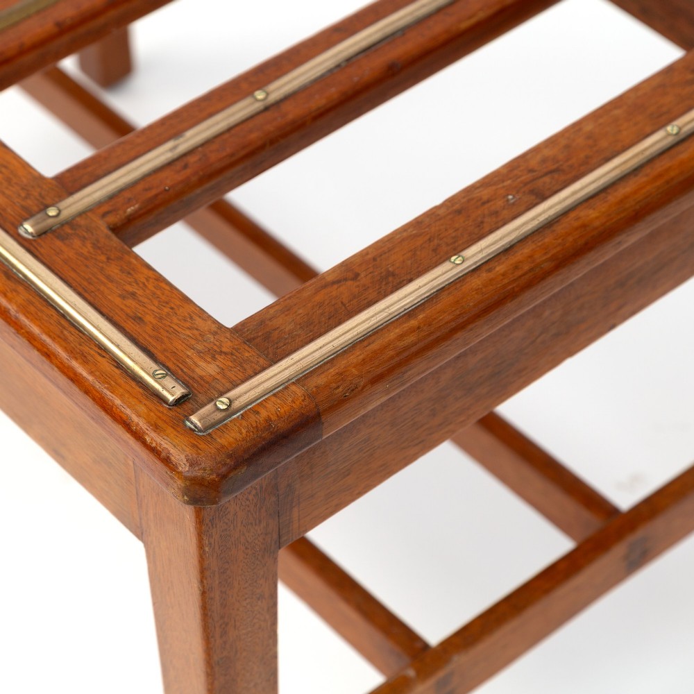 A low rectangular polished oak luggage stand featuring slatted timber top rails inset with protective brass strips supported by four square tapered legs. View V