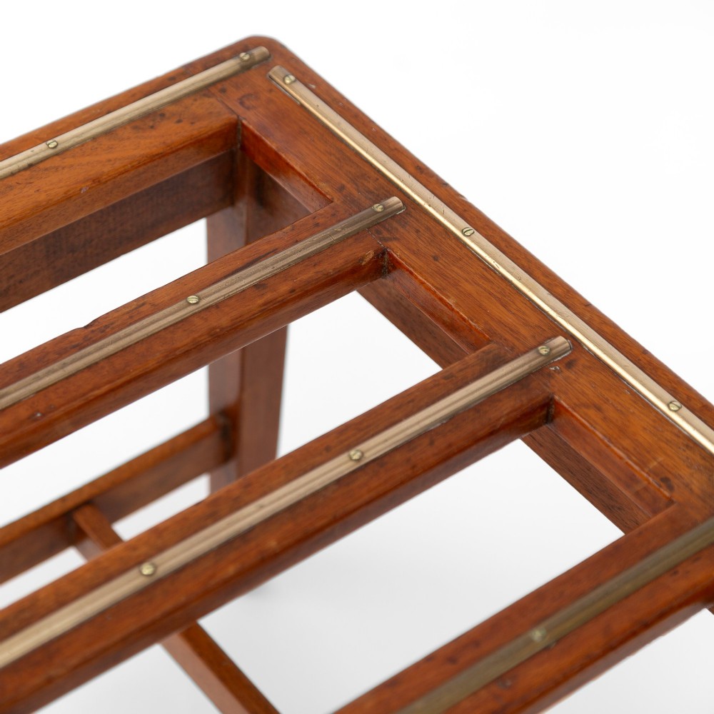 A low rectangular polished oak luggage stand featuring slatted timber top rails inset with protective brass strips supported by four square tapered legs. View VI