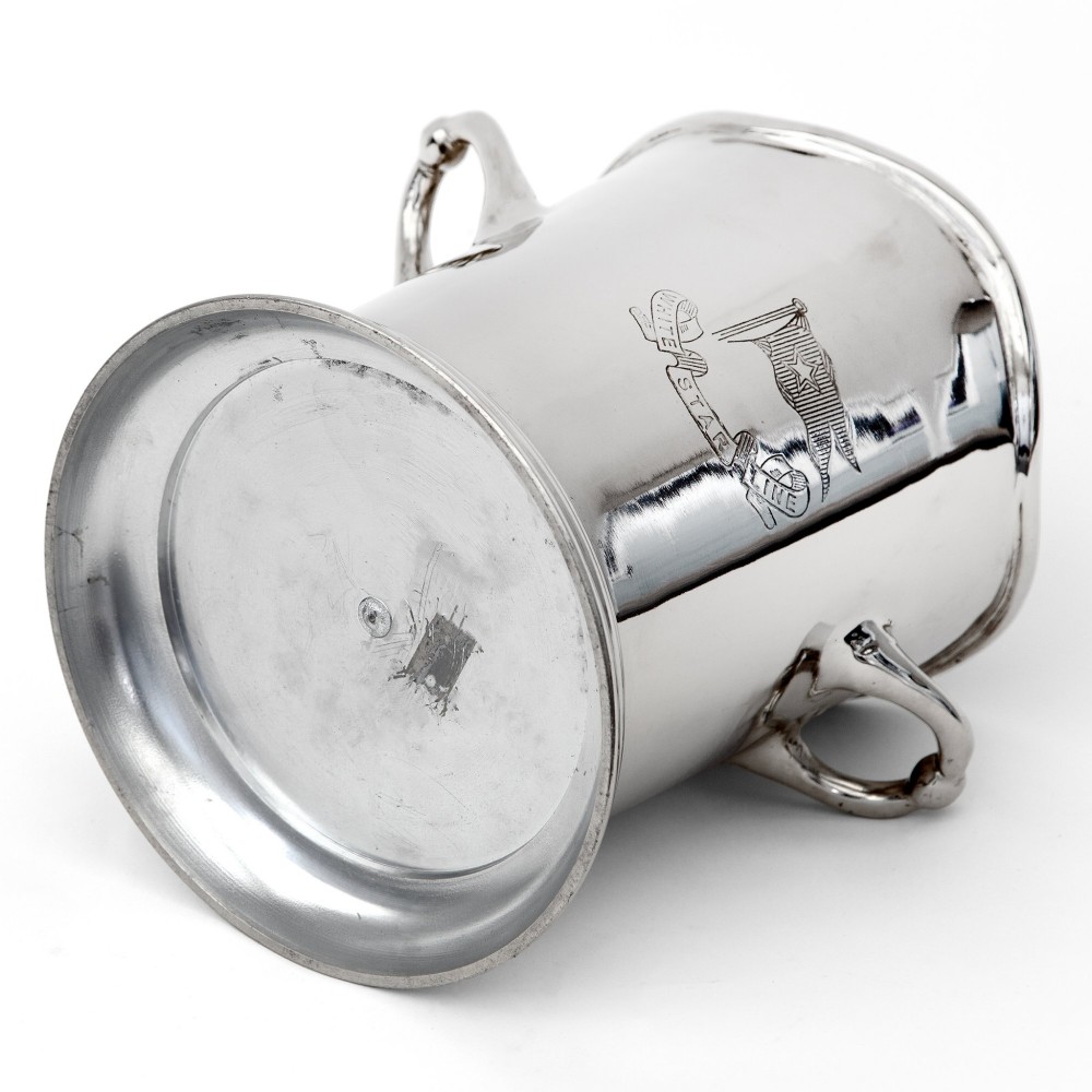 A silver-plated twin-handled wine cooler featuring a shaped rim, stepped base, and an engraved flag logo on the side. View IV