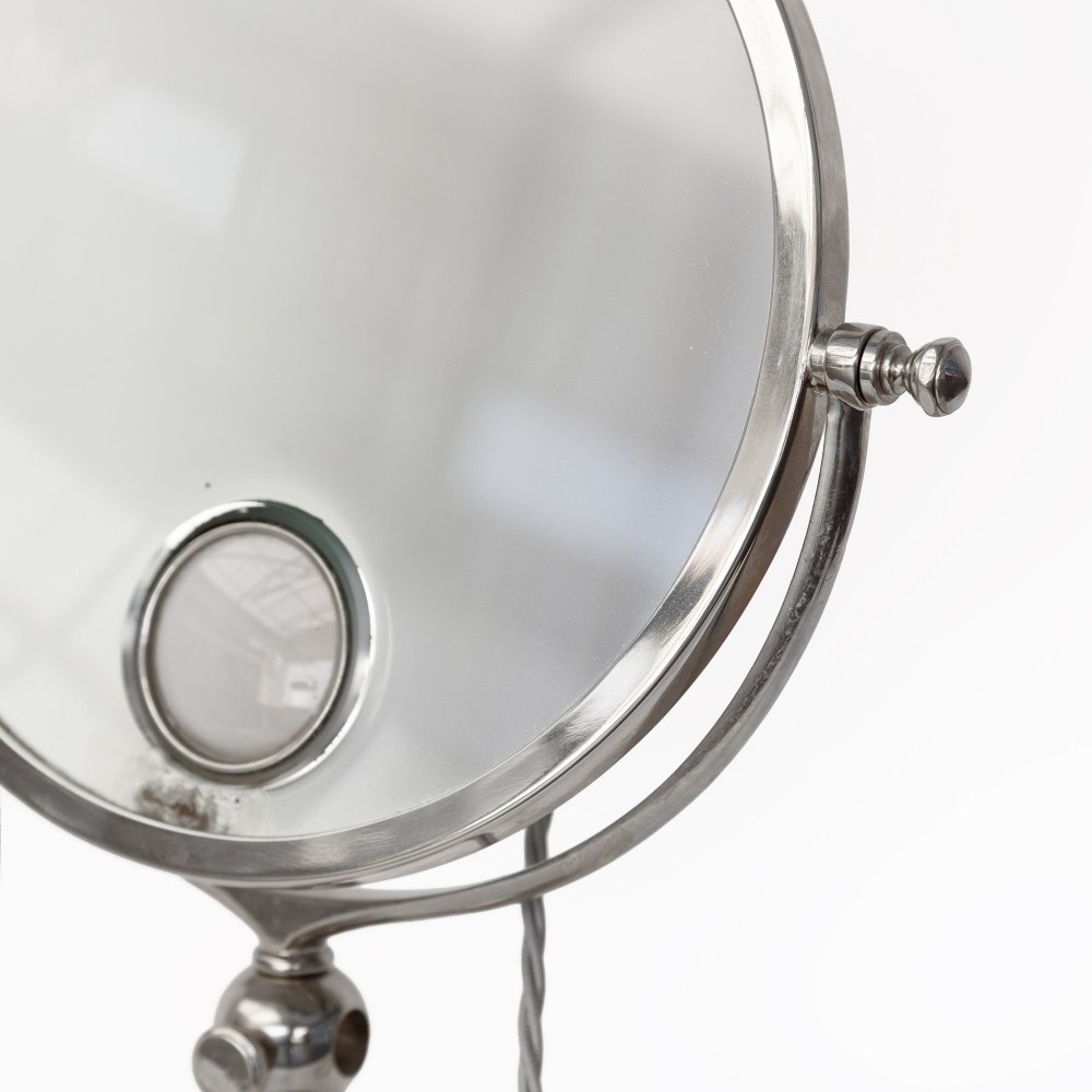 A nickel-plated circular vanity mirror featuring an adjustable swivel stem, circular weighted base, integrated central lens, and braided electrical cord. View IV