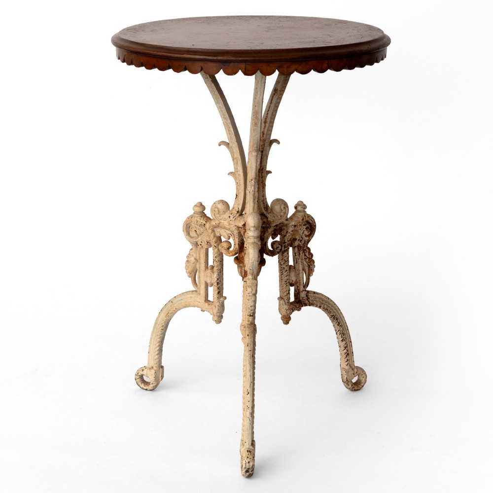 A Victorian cast iron tripod table featuring an off-white painted base with scroll motifs and a circular dark wood top with a scalloped edge. View II