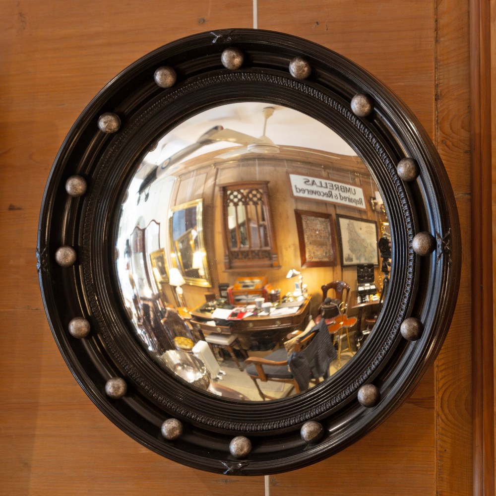 A circular ebonised wall mirror featuring convex glass enclosed in a molded black frame with spherical silver accents.