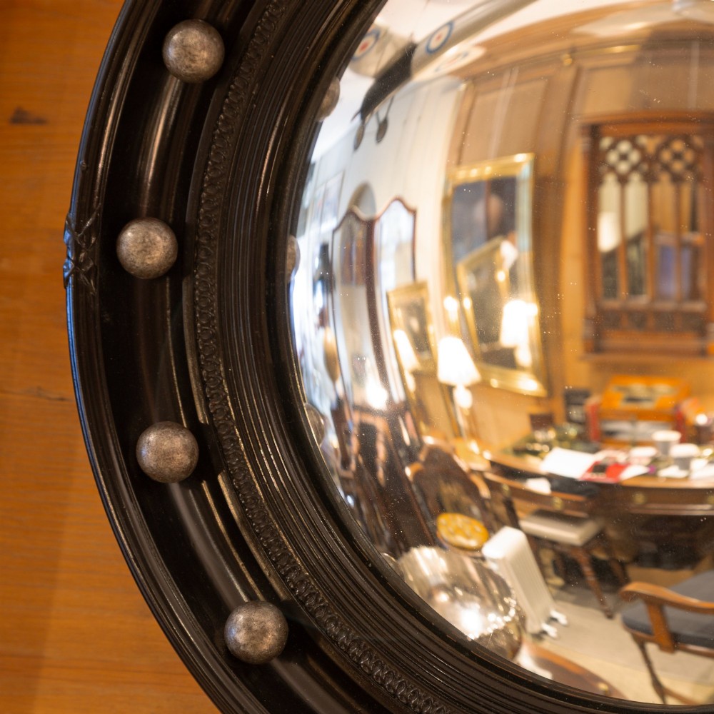 A circular ebonised wall mirror featuring convex glass enclosed in a molded black frame with spherical silver accents. View II