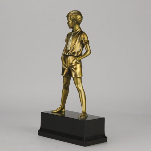 fig 1. An Art Deco bronze sculpture depicting a standing young boy with hands in his pockets, mounted on a rectangular black marble plinth.