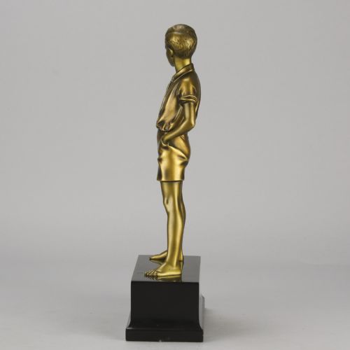 fig 2. An Art Deco bronze sculpture depicting a standing young boy with hands in his pockets, mounted on a rectangular black marble plinth.
