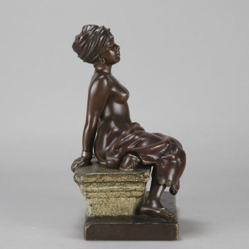 fig 3. A dark brown patinated bronze sculpture of a seated figure wearing a headwrap and draped skirt, resting on a textured base.
