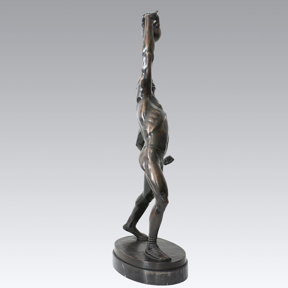 An Art Deco dark patinated bronze sculpture depicting a muscular male figure lifting a weight overhead on an oval dark base.