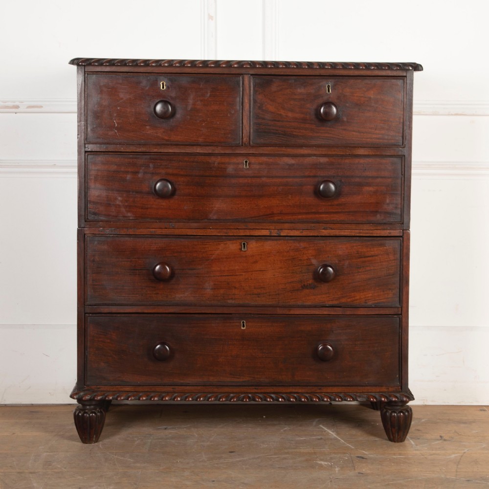 An early nineteenth-century dark padouk wood campaign chest of drawers featuring turned handles, brass escutcheons, carved gadrooned borders, and turned feet.