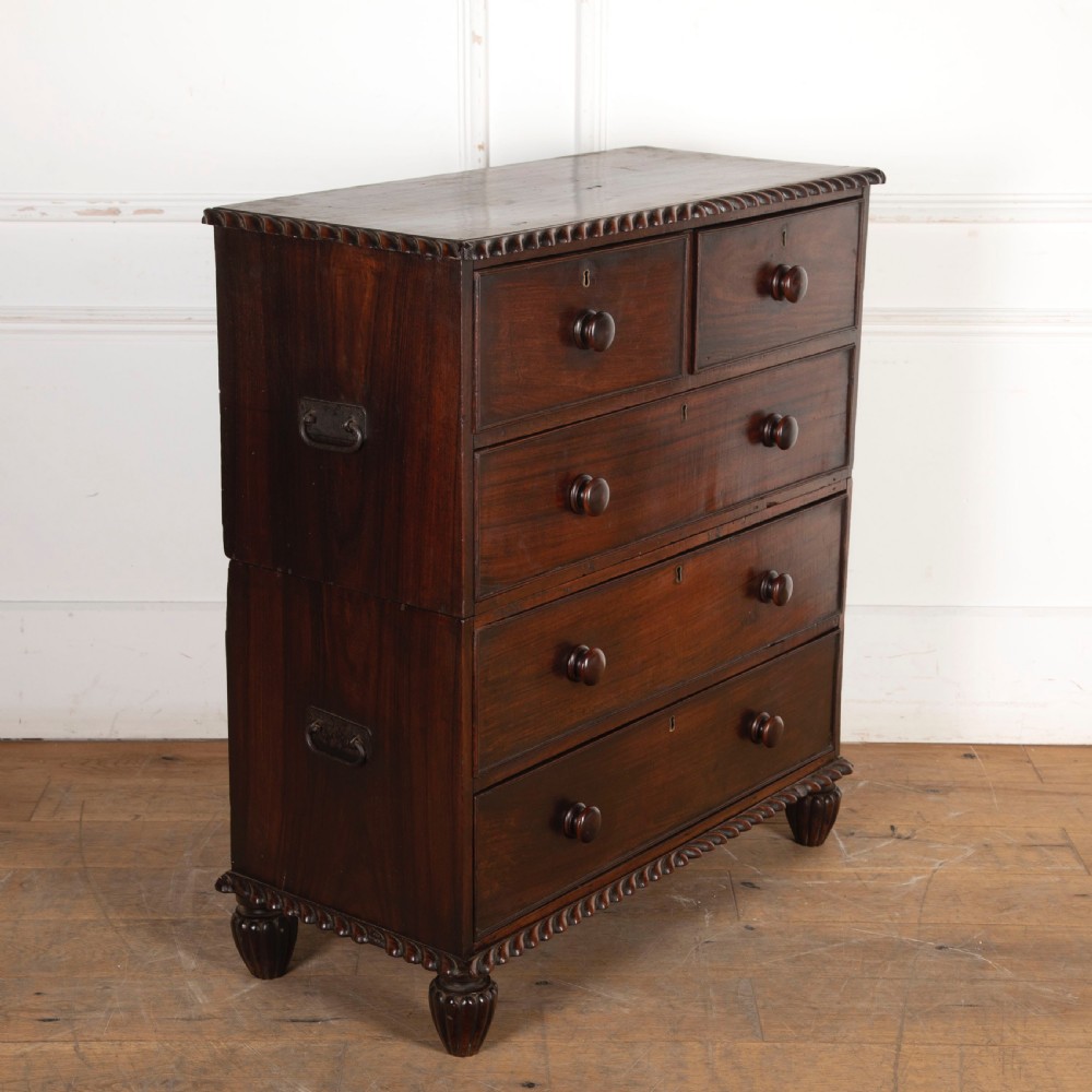 An early nineteenth-century dark padouk wood campaign chest of drawers featuring turned handles, brass escutcheons, carved gadrooned borders, and turned feet. View II