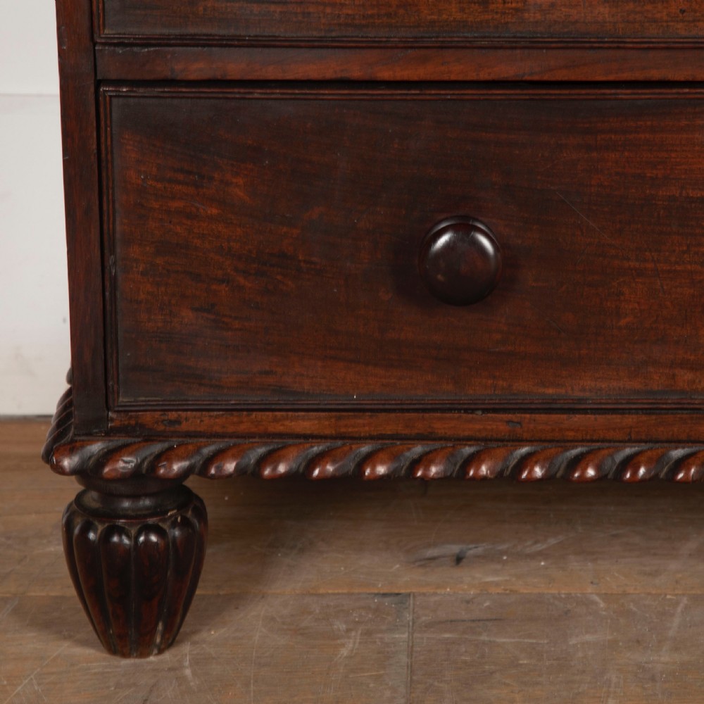 An early nineteenth-century dark padouk wood campaign chest of drawers featuring turned handles, brass escutcheons, carved gadrooned borders, and turned feet. View III