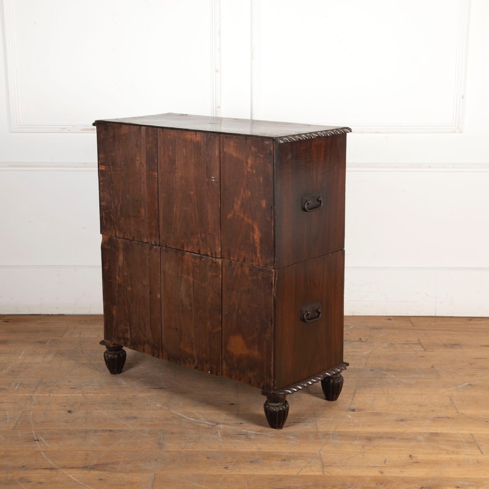An early nineteenth-century dark padouk wood campaign chest of drawers featuring turned handles, brass escutcheons, carved gadrooned borders, and turned feet. View V