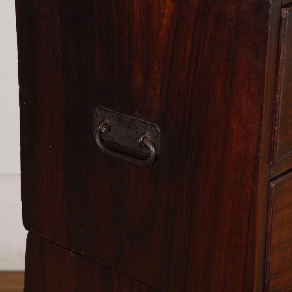 An early nineteenth-century dark padouk wood campaign chest of drawers featuring turned handles, brass escutcheons, carved gadrooned borders, and turned feet. View VI