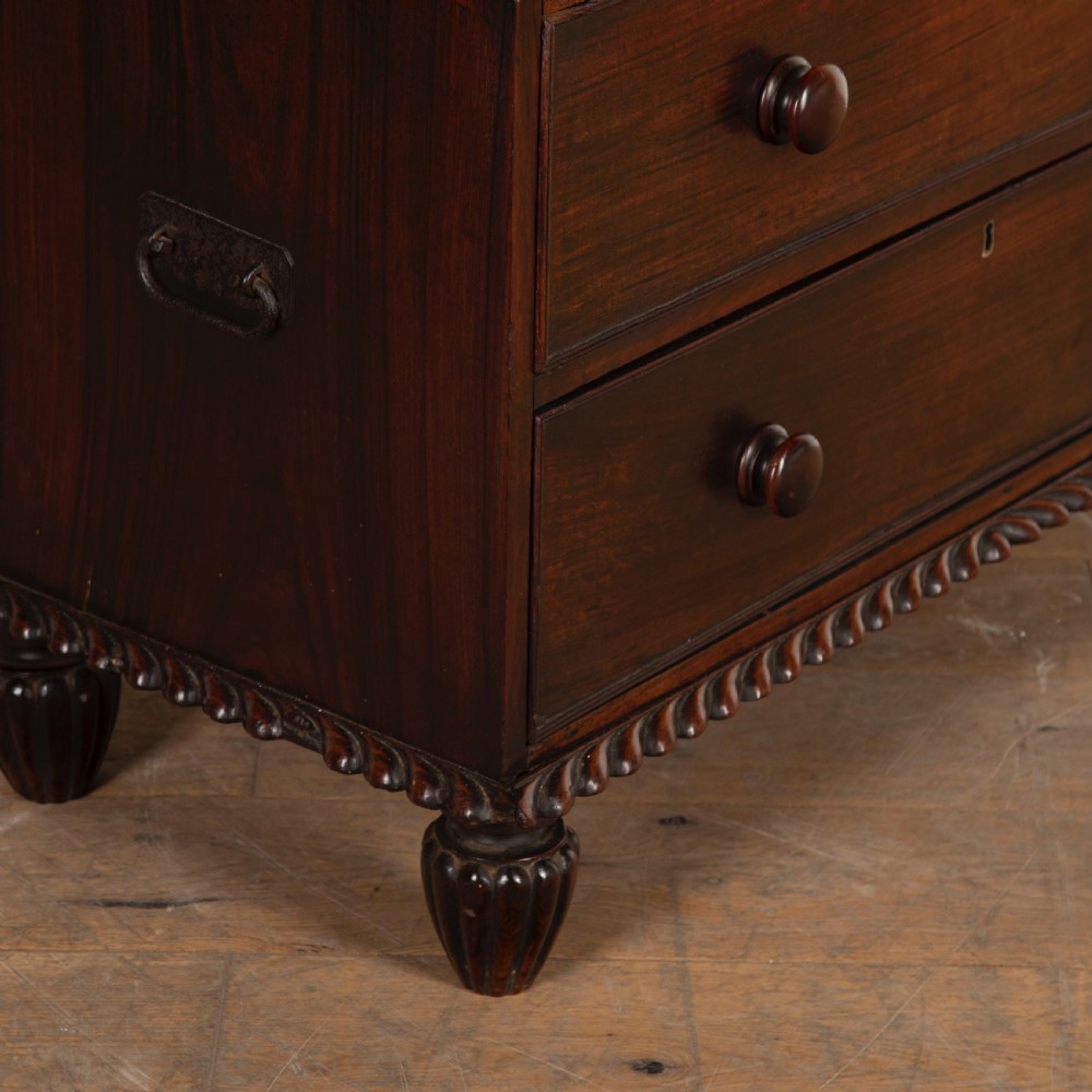 An early nineteenth-century dark padouk wood campaign chest of drawers featuring turned handles, brass escutcheons, carved gadrooned borders, and turned feet. View IX