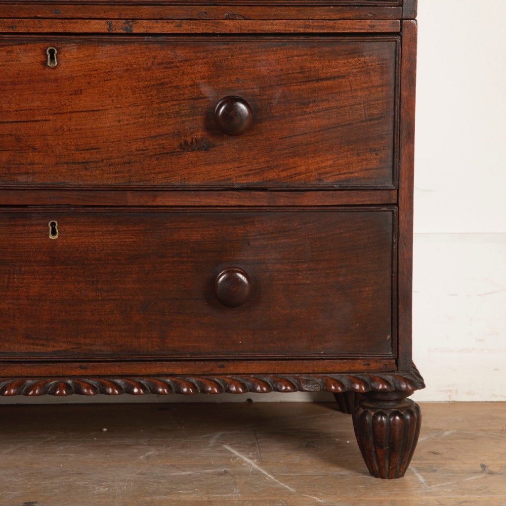 An early nineteenth-century dark padouk wood campaign chest of drawers featuring turned handles, brass escutcheons, carved gadrooned borders, and turned feet. View X